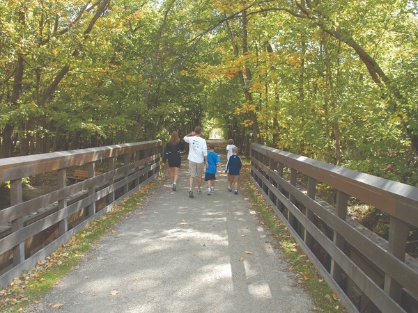 Family walks across a bridge over the Clinton River into a wooded path