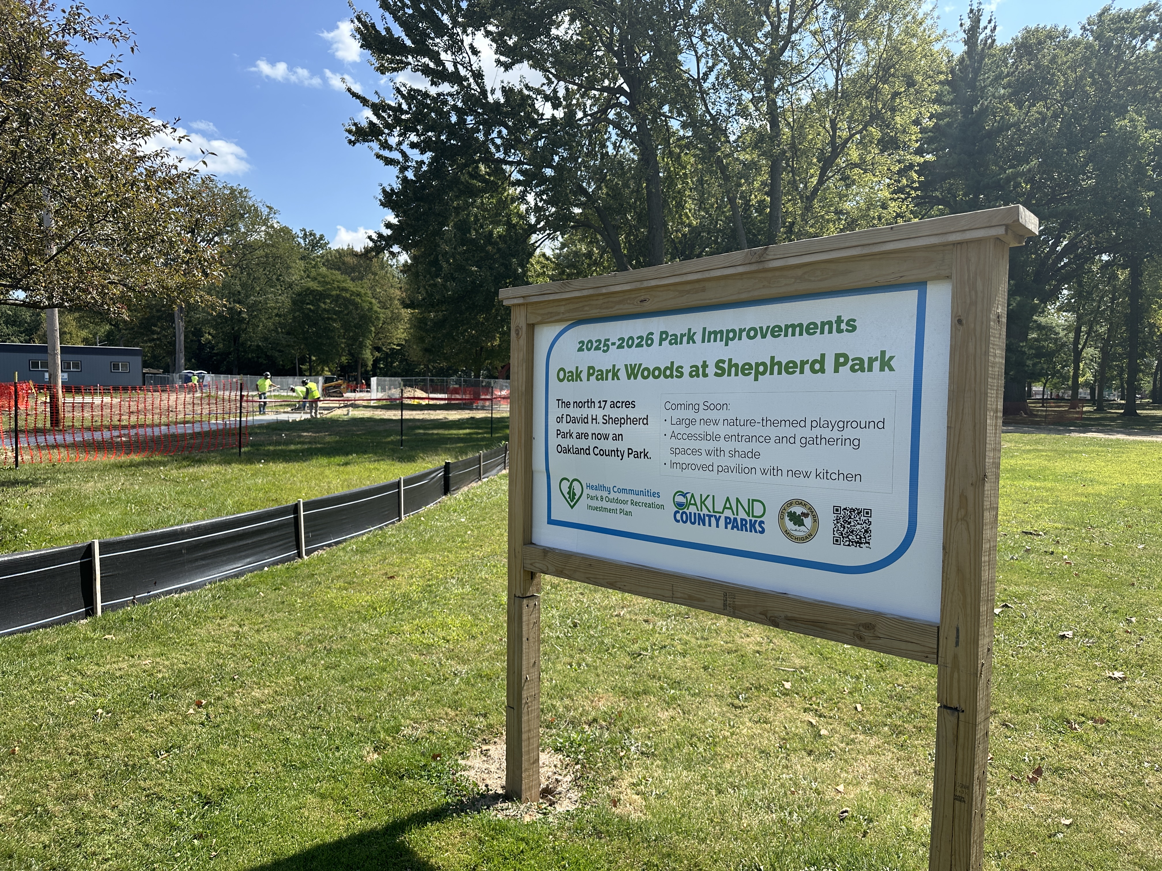 a sign at the park describing the improvements that will be made, with construction happening in the background