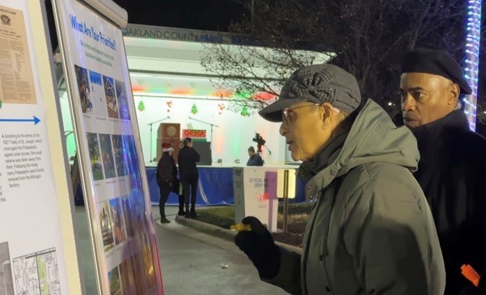 two people standing before a sign at a public open house event at night