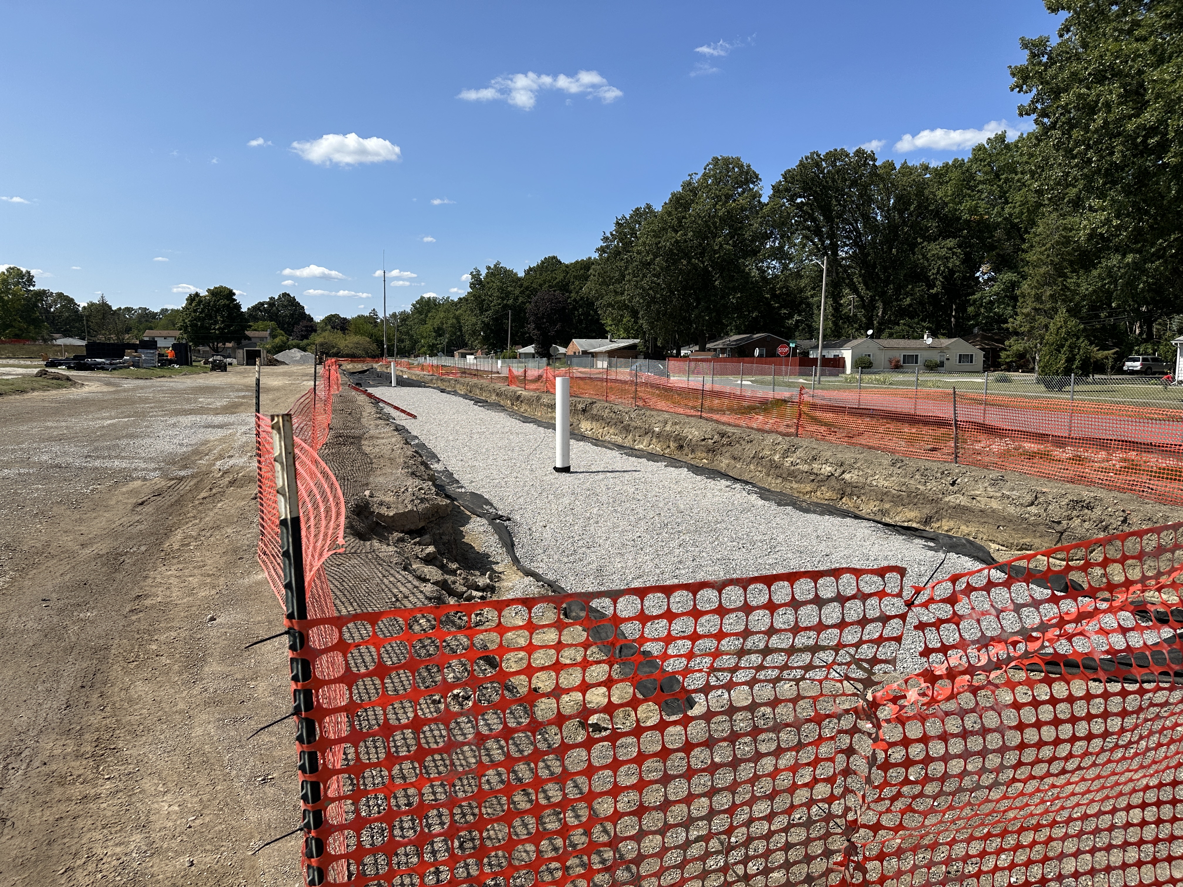 temporary orange fencing surrounding an active construction site, a long hole dug out of the ground